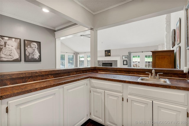 9622 S Maplewood Ave, Tulsa, OK 74137 - kitchen with dark countertops, a ceiling fan, white cabinetry, a stone fireplace, and vaulted ceiling