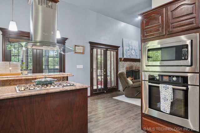 10102 N 147th E Ave, Owasso, OK 74055 - kitchen featuring stainless steel appliances, island exhaust hood, wood finished floors, a fireplace, and dark brown cabinetry