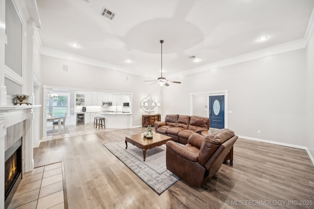 4852 E Redbud Dr, Claremore, OK 74019 - living area featuring a tiled fireplace, light wood finished floors, a ceiling fan, wine cooler, and crown molding
