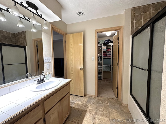 1530 Persimmon, Ardmore, OK 73401 - full bathroom with an enclosed shower, vanity, a walk in closet, a textured ceiling, and stone finish floors