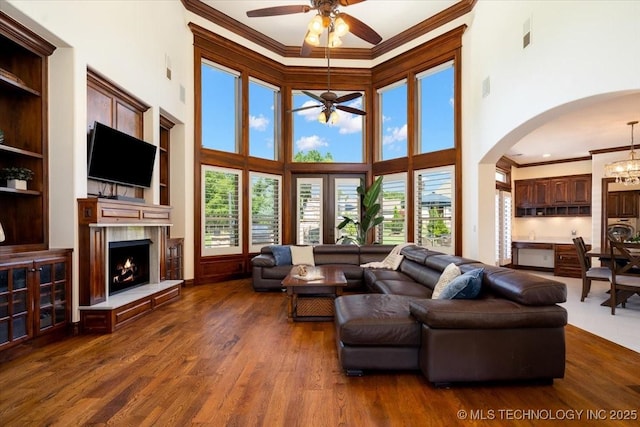 6797 Hummingbird Ct, Owasso, OK 74055 - living room with crown molding, a ceiling fan, dark wood-type flooring, a warm lit fireplace, and arched walkways