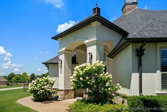 6797 Hummingbird Ct, Owasso, OK 74055 - doorway to property featuring a lawn, stucco siding, a shingled roof, and a chimney