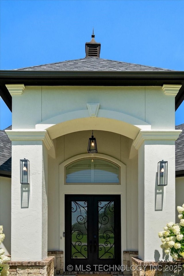 6797 Hummingbird Ct, Owasso, OK 74055 - view of exterior entry featuring french doors, a shingled roof, and stucco siding