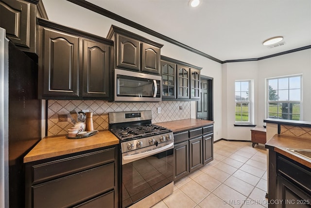 1018 W Evergreen St, Skiatook, OK 74070 - kitchen featuring appliances with stainless steel finishes, decorative backsplash, ornamental molding, light tile patterned floors, and glass insert cabinets