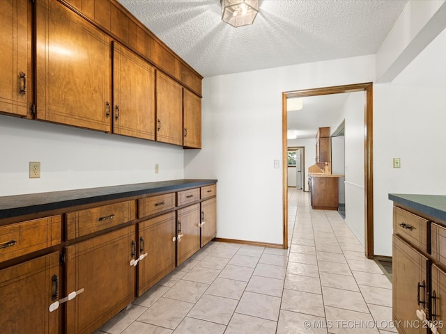 317 NE Autumn Ct, Bartlesville, OK 74006 - kitchen featuring brown cabinets, dark countertops, light tile patterned flooring, and a textured ceiling