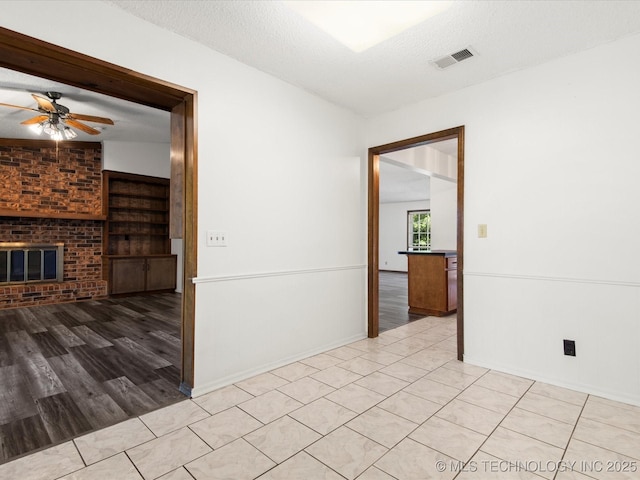 317 NE Autumn Ct, Bartlesville, OK 74006 - spare room featuring a ceiling fan, a textured ceiling, a brick fireplace, and wood finished floors