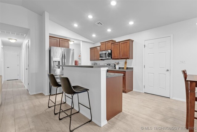 8745 S 261st E Ave, Broken Arrow, OK 74014 - kitchen featuring appliances with stainless steel finishes, a breakfast bar area, vaulted ceiling, light wood-style floors, and brown cabinetry