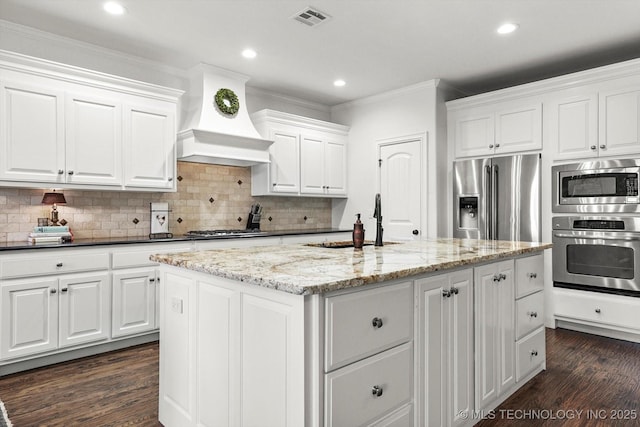 11248 S 75th Ave E, Bixby, OK 74008 - kitchen featuring appliances with stainless steel finishes, custom range hood, crown molding, dark wood finished floors, and white cabinets