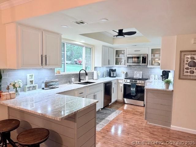 31990 S 624th Pl Unit 65, Grove, OK 74344 - kitchen featuring appliances with stainless steel finishes, a peninsula, a kitchen bar, light stone countertops, and glass insert cabinets
