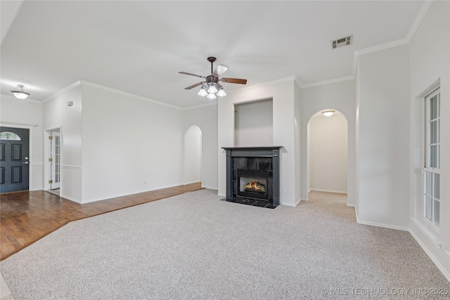 2629 S 13th St, Broken Arrow, OK 74012 - unfurnished living room featuring arched walkways, crown molding, a ceiling fan, carpet flooring, and a tile fireplace