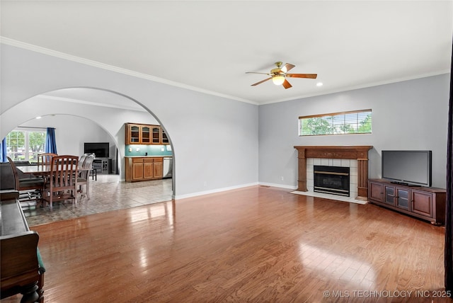 10672 E Canyon Oaks Ct, Claremore, OK 74017 - unfurnished living room with a tile fireplace, ceiling fan, wood finished floors, arched walkways, and ornamental molding