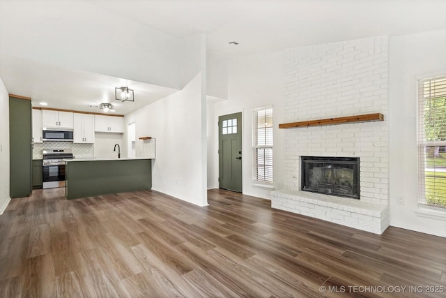 1847 W 57th Pl, Tulsa, OK 74107 - unfurnished living room featuring healthy amount of natural light, dark wood-style floors, and a brick fireplace