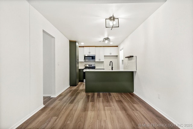 1847 W 57th Pl, Tulsa, OK 74107 - kitchen with stainless steel appliances, a peninsula, wood finished floors, backsplash, and white cabinets