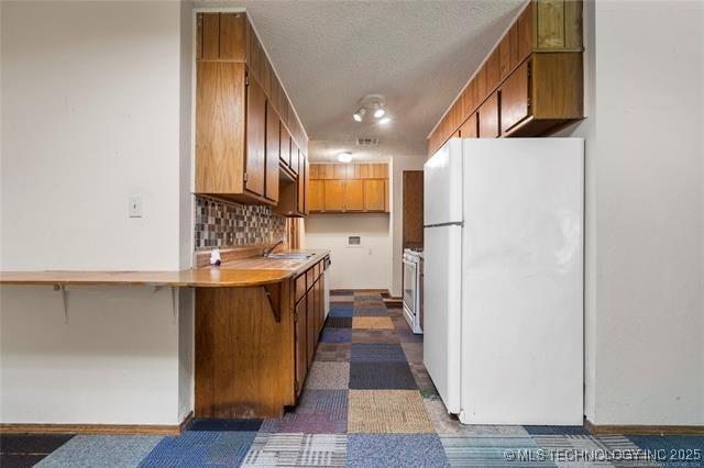 2608 Hickory Bluff Rd, Sapulpa, OK 74066 - kitchen with freestanding refrigerator, brown cabinetry, light countertops, stove, and tasteful backsplash