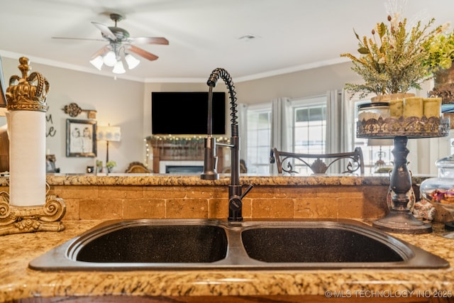 8702 N 140th Ter, Owasso, OK 74055 - kitchen featuring a fireplace, a ceiling fan, ornamental molding, and light stone countertops