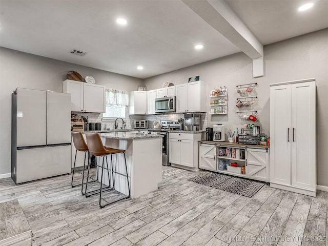 310 W Lee Ave, Sapulpa, OK 74066 - kitchen with appliances with stainless steel finishes, a breakfast bar, light wood-type flooring, backsplash, and white cabinets
