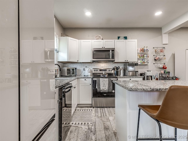 310 W Lee Ave, Sapulpa, OK 74066 - kitchen with appliances with stainless steel finishes, white cabinetry, decorative backsplash, a breakfast bar area, and light stone countertops