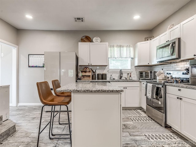310 W Lee Ave, Sapulpa, OK 74066 - kitchen featuring appliances with stainless steel finishes, backsplash, a kitchen island, a kitchen breakfast bar, and light stone countertops
