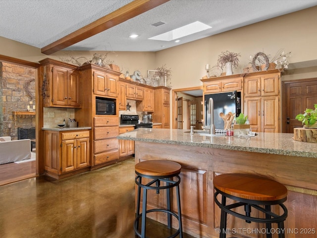 6429 Clear Creek Loop, Bartlesville, OK 74006 - kitchen featuring black appliances, a textured ceiling, a skylight, a stone fireplace, and a breakfast bar area