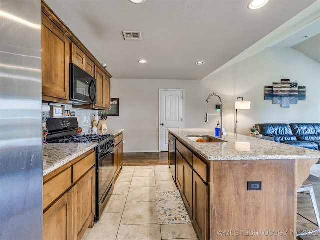 3409 E Quebec St, Broken Arrow, OK 74014 - kitchen featuring black appliances, light stone counters, a kitchen island with sink, recessed lighting, and brown cabinets