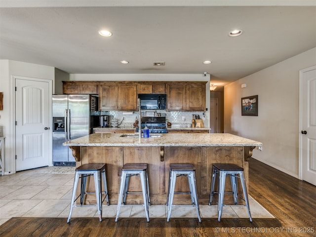 3409 E Quebec St, Broken Arrow, OK 74014 - kitchen featuring black microwave, stainless steel fridge with ice dispenser, a kitchen bar, light stone countertops, and decorative backsplash