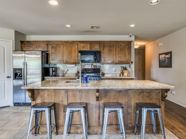 3409 E Quebec St, Broken Arrow, OK 74014 - kitchen with black microwave, stainless steel refrigerator with ice dispenser, tasteful backsplash, light stone counters, and a kitchen breakfast bar