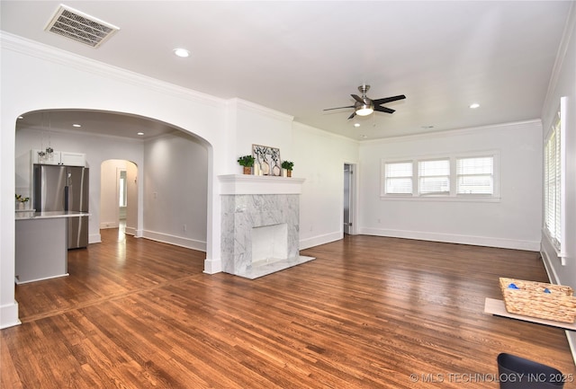2020 E 14th St, Tulsa, OK 74104 - unfurnished living room featuring a ceiling fan, arched walkways, dark wood-type flooring, ornamental molding, and a premium fireplace
