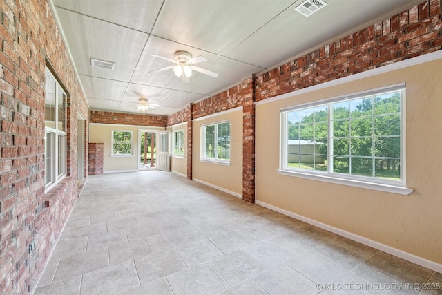 1701 N Skinner Ave, Drumright, OK 74030 - unfurnished sunroom featuring ceiling fan, healthy amount of natural light, brick wall, and stone finish floors