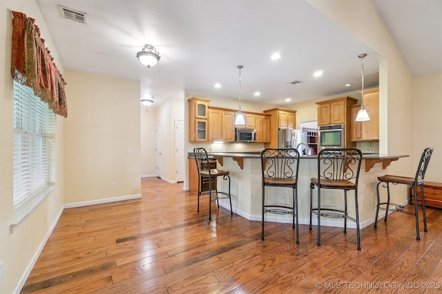 1701 N Skinner Ave, Drumright, OK 74030 - kitchen with stainless steel appliances, a peninsula, dark countertops, a breakfast bar area, and light wood-style flooring
