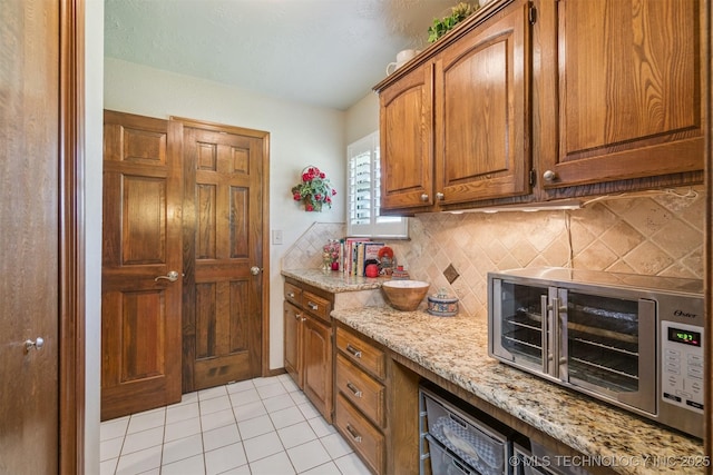 1605 N Skinner Ave, Drumright, OK 74030 - kitchen featuring decorative backsplash, light tile patterned flooring, light stone countertops, brown cabinetry, and stainless steel microwave