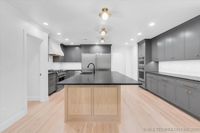 4155 S Birmingham Pl, Tulsa, OK 74105 - kitchen with high end appliances, custom exhaust hood, light wood-style floors, dark countertops, and a center island with sink