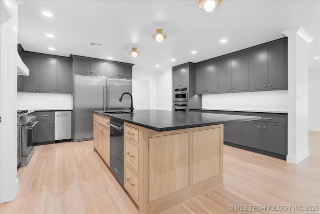 4155 S Birmingham Pl, Tulsa, OK 74105 - kitchen featuring high quality appliances, light wood finished floors, light brown cabinetry, tasteful backsplash, and a kitchen island with sink