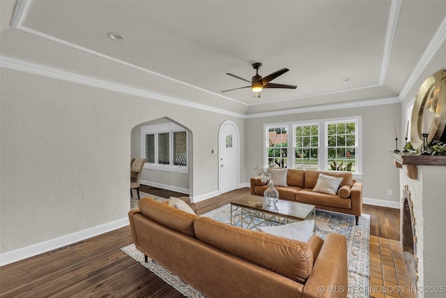 1743 S Florence Pl, Tulsa, OK 74104 - living room featuring arched walkways, ceiling fan, a raised ceiling, dark wood-type flooring, and crown molding