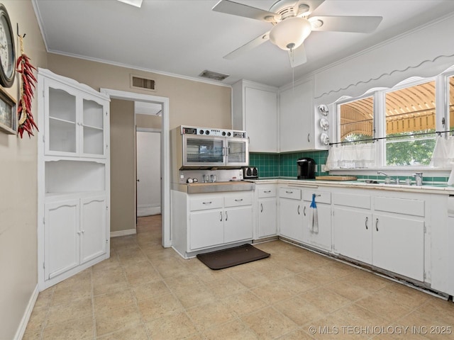 320 E 7th St, Pawhuska, OK 74056 - kitchen with decorative backsplash, white cabinets, a ceiling fan, light countertops, and ornamental molding