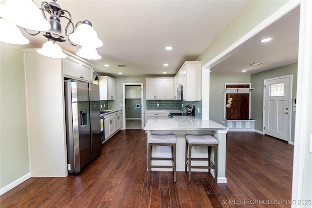 410 Denver St, Pawnee, OK 74058 - kitchen featuring appliances with stainless steel finishes, a peninsula, backsplash, dark wood-type flooring, and a kitchen breakfast bar