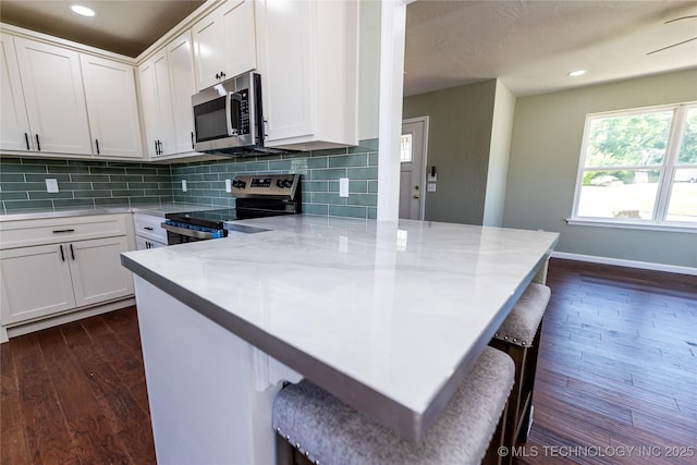 410 Denver St, Pawnee, OK 74058 - kitchen with appliances with stainless steel finishes, a peninsula, dark wood finished floors, a breakfast bar area, and tasteful backsplash
