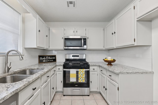 2244 W 45th St, Tulsa, OK 74107 - kitchen featuring appliances with stainless steel finishes, white cabinetry, light tile patterned flooring, a textured ceiling, and light stone countertops