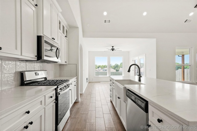 2916 S 8th St, Broken Arrow, OK 74012 - kitchen featuring stainless steel appliances, backsplash, white cabinets, light stone counters, and a kitchen island with sink