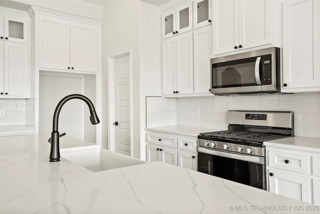 2916 S 8th St, Broken Arrow, OK 74012 - kitchen with appliances with stainless steel finishes, white cabinetry, decorative backsplash, and glass insert cabinets