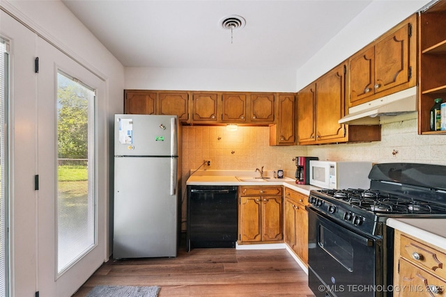 2321 S Main St, Sapulpa, OK 74066 - kitchen featuring black appliances, under cabinet range hood, light countertops, brown cabinetry, and backsplash