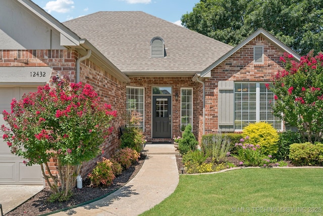 12432 S 101st E Ave, Bixby, OK 74008 - view of exterior entry with brick siding, roof with shingles, a yard, and a garage