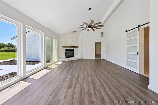 13973 S 237th E Ave, Coweta, OK 74429 - unfurnished living room featuring a barn door, wood finished floors, a stone fireplace, ceiling fan, and high vaulted ceiling