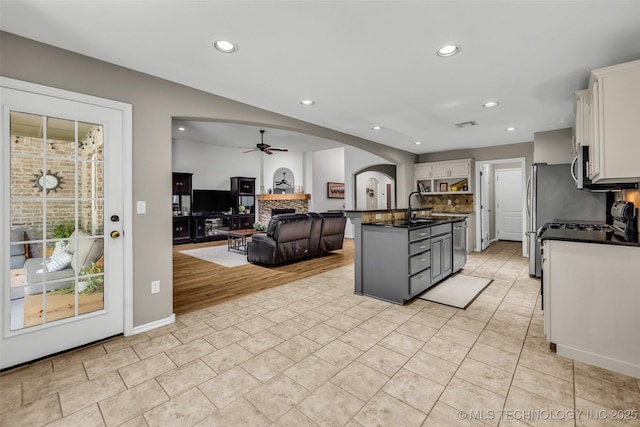1116 W Fargo Dr, Broken Arrow, OK 74012 - kitchen featuring a ceiling fan, a fireplace, dark countertops, arched walkways, and white cabinetry