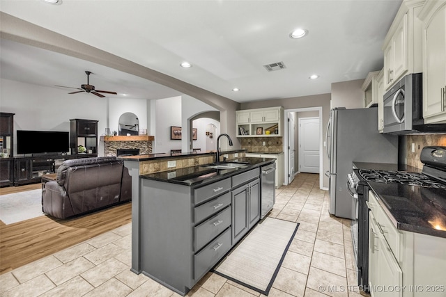 1116 W Fargo Dr, Broken Arrow, OK 74012 - kitchen featuring appliances with stainless steel finishes, arched walkways, a fireplace, a ceiling fan, and decorative backsplash