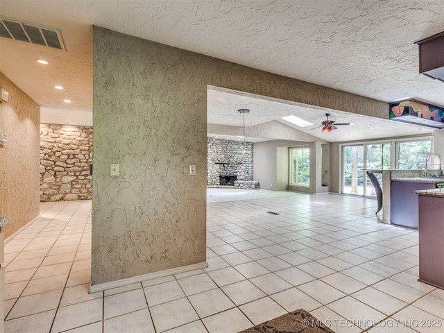 5704 E 65th St, Tulsa, OK 74136 - unfurnished living room featuring a stone fireplace, ceiling fan, healthy amount of natural light, light tile patterned flooring, and a textured ceiling