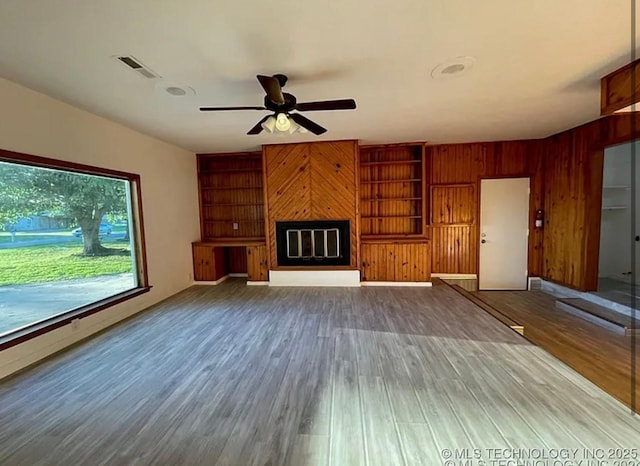 802 N Main St, Wagoner, OK 74467 - unfurnished living room with a ceiling fan, a glass covered fireplace, wood finished floors, built in features, and wood walls