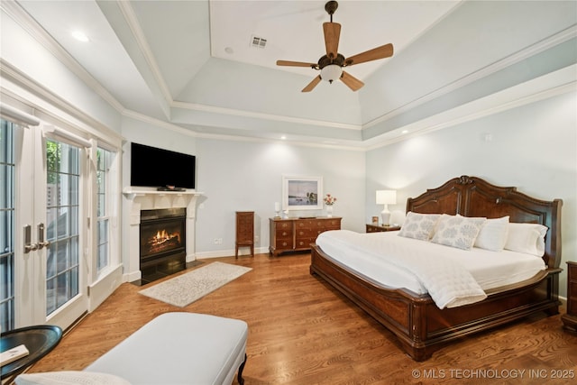 8002 E Galveston Pl, Broken Arrow, OK 74014 - bedroom featuring a tray ceiling, a fireplace with flush hearth, wood finished floors, access to exterior, and ceiling fan