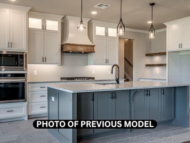 7010 E 137th St, Collinsville, OK 74021 - kitchen with stainless steel appliances, premium range hood, white cabinetry, crown molding, and a center island with sink