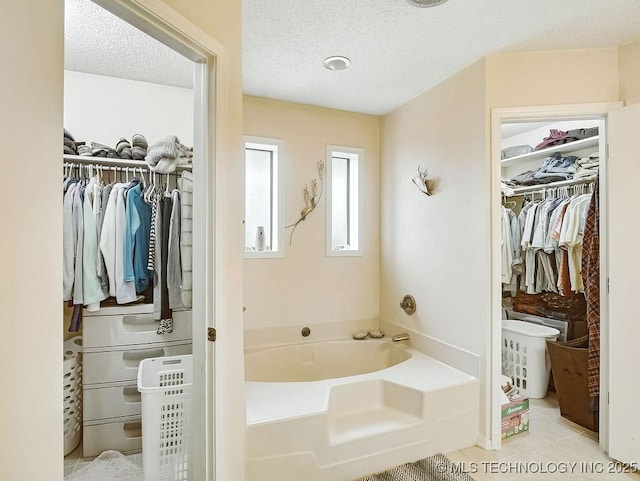 301 S Byrd, Coalgate, OK 74538 - bathroom featuring a garden tub, a spacious closet, a textured ceiling, and tile patterned floors
