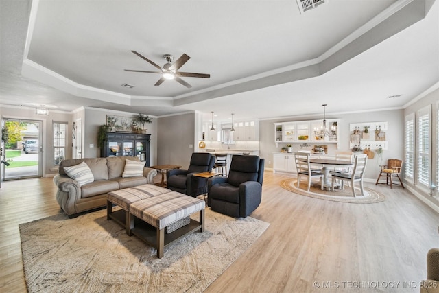 12708 E 78th St, Owasso, OK 74055 - living area featuring a tray ceiling, light wood-type flooring, ornamental molding, a ceiling fan, and a chandelier
